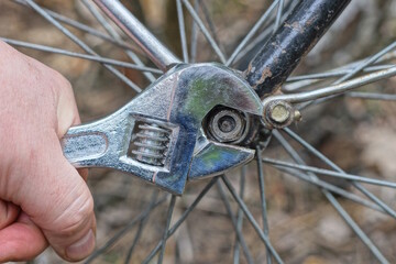 a hand with a gray adjustable wrench tightens a nut on a black frame and a bicycle wheel