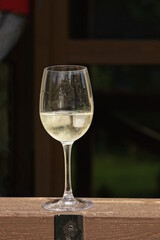 one white glass goblet with yellow wine and pieces of ice stands on a brown wooden table outdoors on a gray background