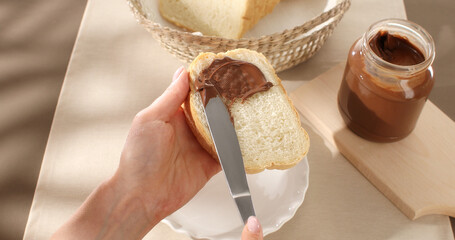 Bread slice with chocolate hazelnut spread or butter. Female hands spreading chocolate butter on sandwich bread by knife. Spreading hazelnut cream, chocolate nut butter. Close up.