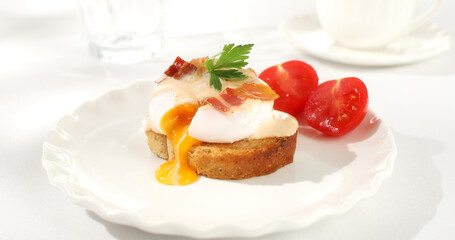 toast with poached egg and bacon on a plate. serving breakfast on a white plate with tomato. sunny day. angle view. 