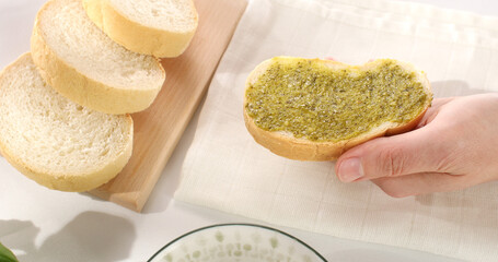 hand holding bread with spreaded pesto. close-up. angle view. making a sandwich. italian sauce....