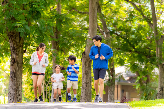 Happy Asian parent and little kids enjoy and fun outdoor lifestyle on summer vacation. Father, mother and child jogging workout exercise together at park. Family relationship and health care concept.