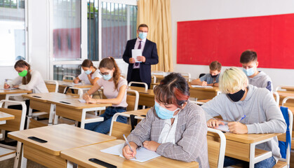 Portrait of focused teenage schoolgirl wearing face mask for protection from virus disease studying in classroom