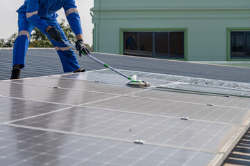 Man using a mop and water to clean the solar panels that are dirty with dust and birds' droppings to improve the efficiency of solar energy storage.