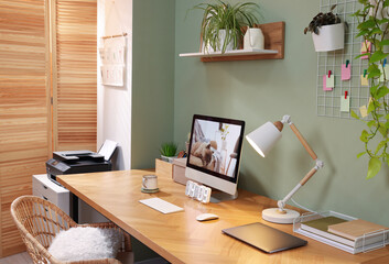Stylish workplace with computer, laptop and lamp near olive wall at home