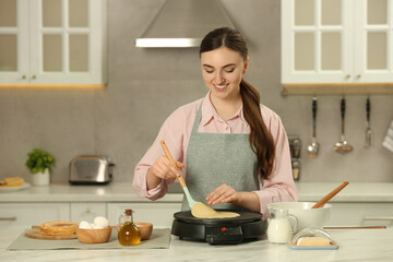 Happy woman cooking delicious crepe on electric maker at white marble table in kitchen - obrazy, fototapety, plakaty
