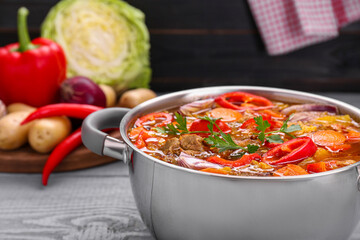 Saucepan of delicious vegetable soup with meat and ingredients on grey wooden table, closeup. Space for text