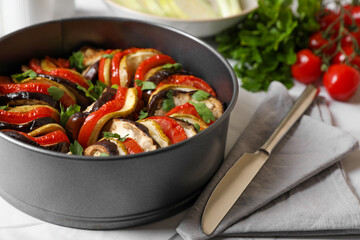 Delicious ratatouille in round baking pan and knife on table, closeup