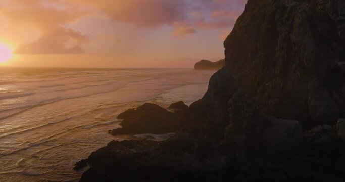 Aerial: Rocky cliff and ocean surf at sunset. 