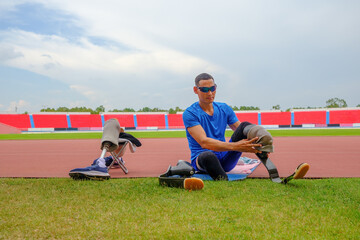 portrait of an Asian paralympic athlete, seated on a stadium track, busily affixing his running...