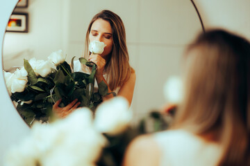 Blissful Bride Smelling White Roses Looking in the Mirror. Beautiful woman enjoying the perfume of...
