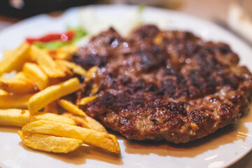 Pljeskavica with french fries on a plate, traditional serbian dish, grilled dish of spiced meat...