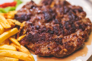 Pljeskavica with french fries on a plate, traditional serbian dish, grilled dish of spiced meat patty mixture of pork, beef and lamb, popular balkan steet food Pleskavitza, served in cafe