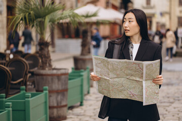 Portrait young asian woman tourist in casual clothes on old city street in europe while checking direction on map