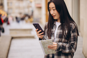 Portrait of a beautiful brunette Korean woman holding a map and comparing it with smartphone navigation on the streets of the old city. Asian tourist woman traveling in Europe.