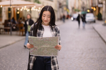 Portrait of a beautiful brunette Korean woman holding a map on the streets of the old city. Asian woman tourist or business lady traveling in Europe.