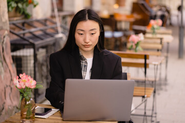 Portrait of a beautiful brunette Korean freelancer sitting in an authentic cafe and using a laptop computer and working on it.