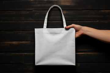 Hand holding a blank white tote bag mockup isolated on black wooden background, eco cotton bag. Generative AI
