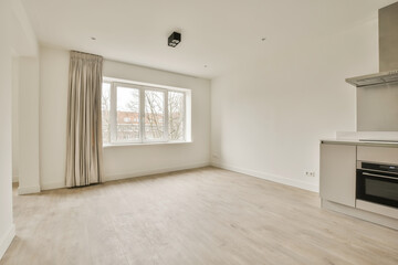 an empty living room with white walls and hardwood flooring in a kitchen area is visible on the right side