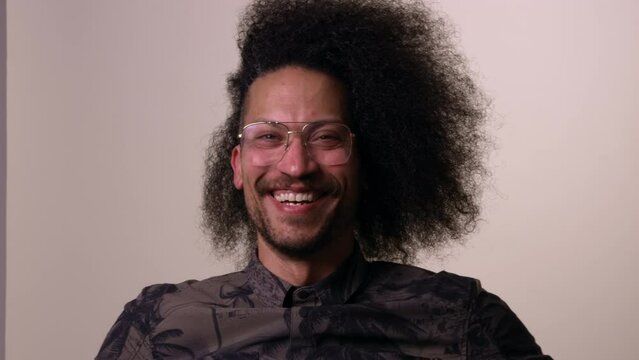 African American man with afro sits in chair and laughs towards camera