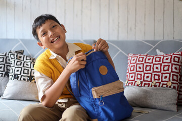 Happy excited elementary schoolboy with his school bag sitting on couch at living room with smile, first day of school. 