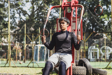 Young fit man working out on chest press machine at park exercising outdoors.