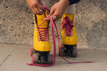 vista desde cerca de manos amarrando unos patines amarillos en la calle con cordones de color fucsia