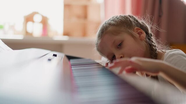Little girl with plaits presses piano keys in living room
