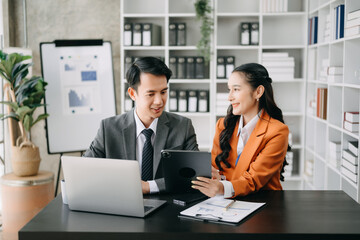 Asian business colleague business presents and explains and using laptop and tablet. Teamwork, financial marketing team, while sitting in home office room.