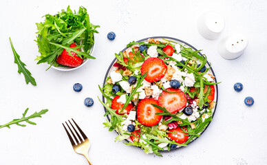 Strawberry salad with arugula, lettuce, blueberries, feta cheese and walnuts, white table. Fresh useful dish for healthy eating