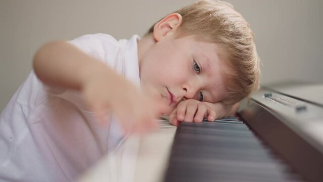 Tired boy presses piano keys in row resting head on keyboard