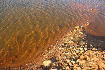 Sandy and rocky shore of a reservoir washed by clear water