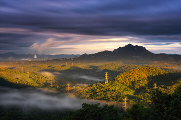 Aerial view Electric pylon in green forest on mountains and fog beautiful golden light in the morning, Concept energy and environment, Lung jaroon view point, Pang Puai, Mae Moh, Lampang, Thailand.