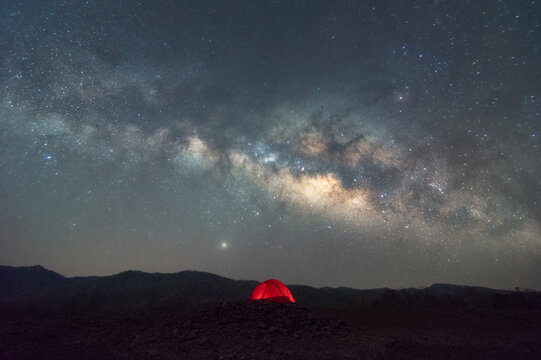 Red tent in reservoir under Milky way galaxy with stars and space dust in the universe, long speed exposure with noise. Baan Sop pat, Mae Moh Lampang Thailand.