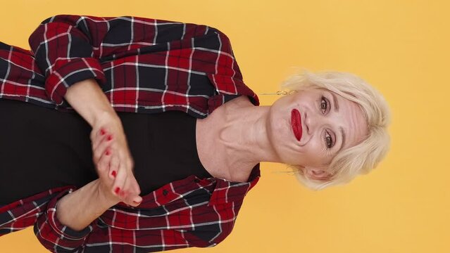 Vertical video. Applauding woman. False congrats. Sarcastic emotion. Skeptic middle-aged lady clapping hands expressing silly joy posing yellow.