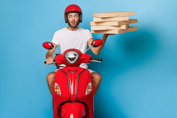 Delivery guy in red helmet rides red scooter on blue background with pack of pizza boxes in one hand, delivery service concept, copy space
