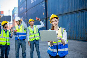 Women worker wear uniform safety helmet using laptop checking containers loading. Area logistics import export and shipping. Female engineering department shipping terminal transportation.