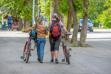 Two women walk with bicycles on the sidewalk on a summer day