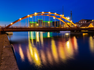 The red semi-circular railway bridge over the canal in Lidkoping in the glowing blue hour lighting and colorful reflections