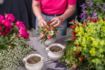 Florist bei der Arbeit, Frau steckt ein Blumengesteck aus frischen bunten Blumen in Gefäße aus Keramik