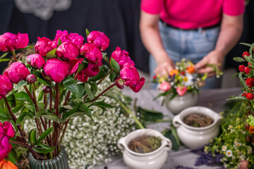 Florist bei der Arbeit, Frau steckt ein Blumengesteck aus frischen bunten Blumen in Gefäße aus Keramik