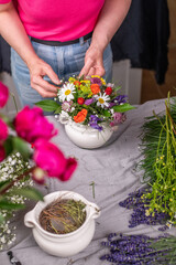 Florist bei der Arbeit, Frau steckt ein Blumengesteck aus frischen bunten Blumen in Gefäße aus Keramik