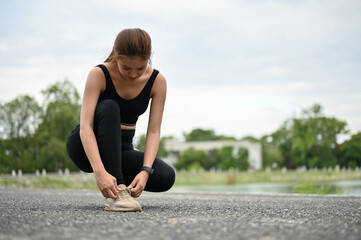 A sporty Asian woman tying her running shoelaces on the street at the public park.
