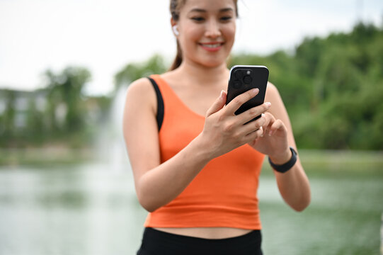 Close-up image of a happy Asian woman choosing a music playlist on her phone before running