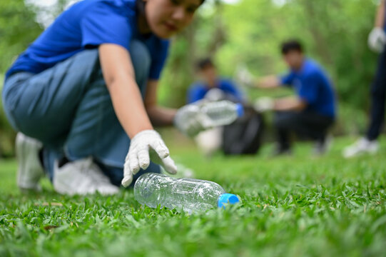 A beautiful Asian female volunteer collecting trash and a plastic bottle in the public park
