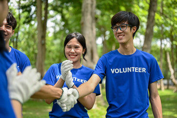 A happy Asian male volunteer shakes hands with his team after finishing volunteer work in the park.