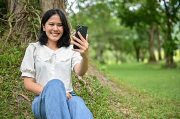 A woman enjoys talking with her friend on a video call while relaxing in a public park.