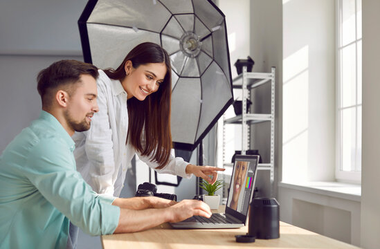 Male photographer and female model choosing photos on laptop together during photoshoot in studio. Couple of professional photographers sitting at laptop computer choosing best photos in office