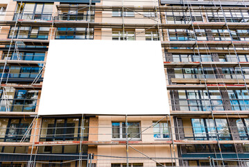 Blank white advertisement hanging on the scaffolding of modern building under construction.Reconstruction of a building with white billboard. - obrazy, fototapety, plakaty