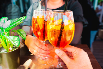 Couple celebratory toast with aperol spritz orange alcoholic cocktails at outdoors cocktail bar at...